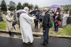 Fête de la Toussaint, prêtre et familles priant au cimetière.