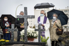 Fête de la Toussaint, prêtre et familles priant au cimetière.