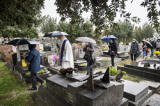 Fête de la Toussaint, prêtre et familles priant au cimetière.