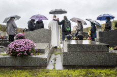 Fête de la Toussaint, prêtre et familles priant au cimetière.