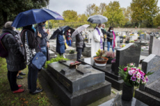 Fête de la Toussaint, prêtre et familles priant au cimetière.