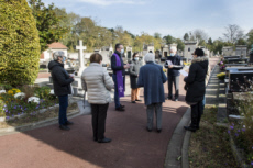 Fête de la Toussaint, prêtre et familles priant dans un cimetière.