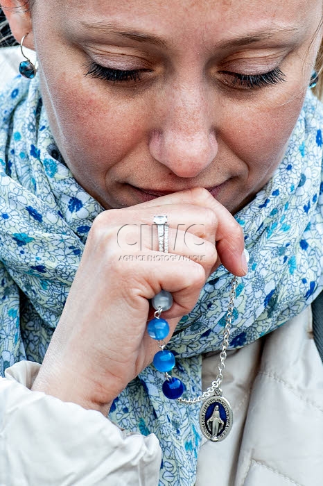 Une jeune femme priant, un chapelet à la main.