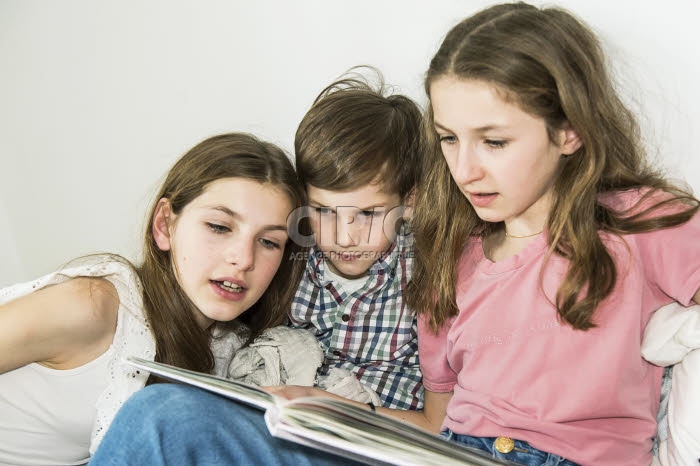 Frère et soeurs lisant un livre ensemble.