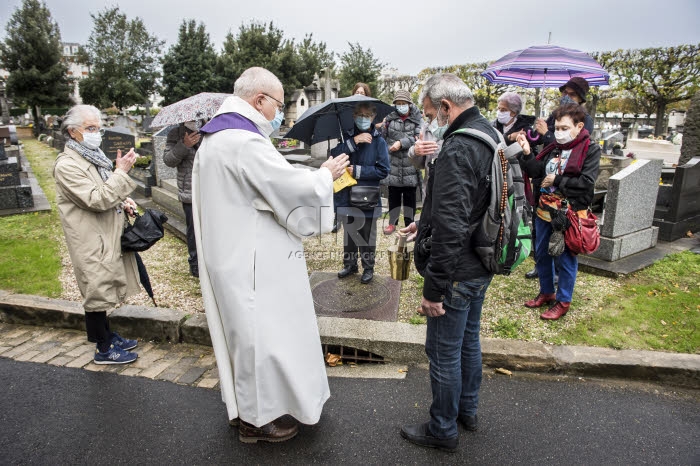 Fête de la Toussaint, prêtre et familles priant au cimetière.