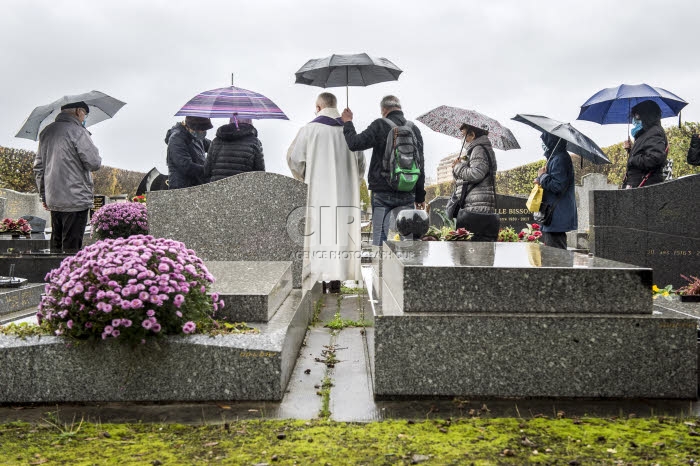 Fête de la Toussaint, prêtre et familles priant au cimetière.