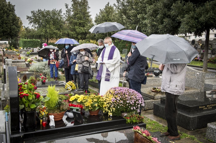 Fête de la Toussaint, prêtre et familles priant au cimetière.