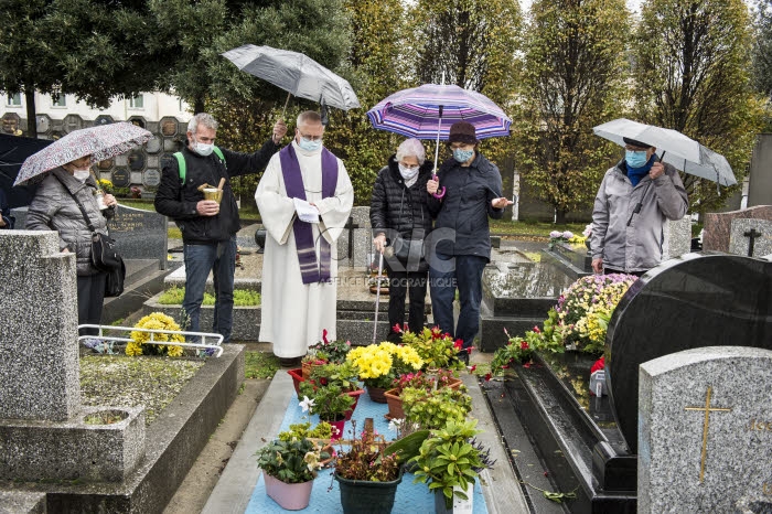 Fête de la Toussaint, prêtre et familles priant au cimetière.