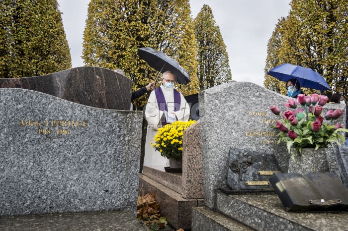 Fête de la Toussaint, prêtre et familles priant au cimetière.