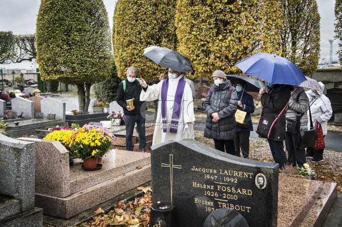 Fête de la Toussaint, prêtre et familles priant au cimetière.