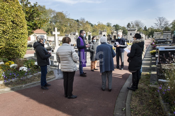 Fête de la Toussaint, prêtre et familles priant dans un cimetière.