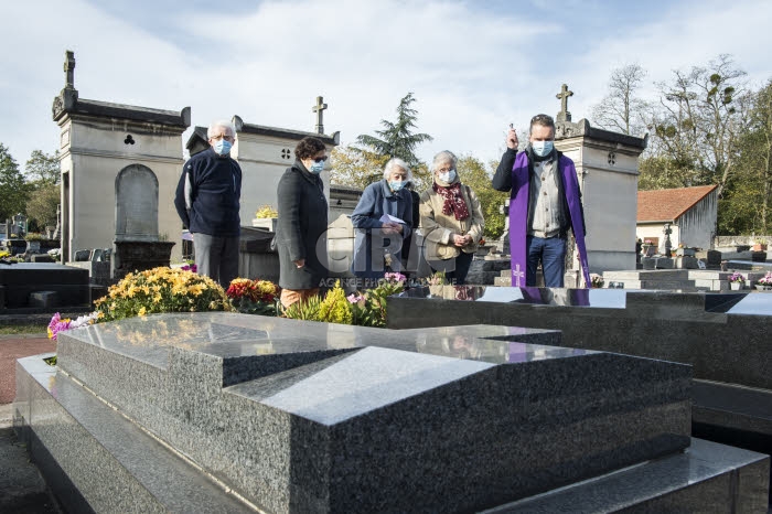 Fête de la Toussaint, prêtre et familles priant dans un cimetière.