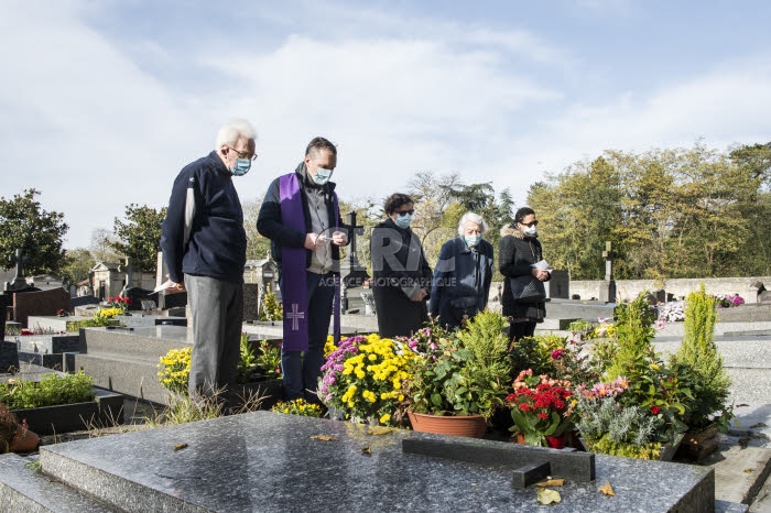 Fête de la Toussaint, prêtre et familles priant dans un cimetière.