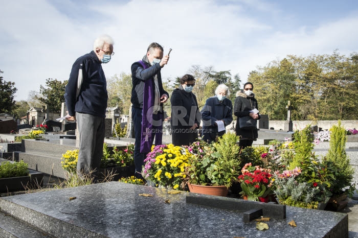 Fête de la Toussaint, prêtre et familles priant dans un cimetière.