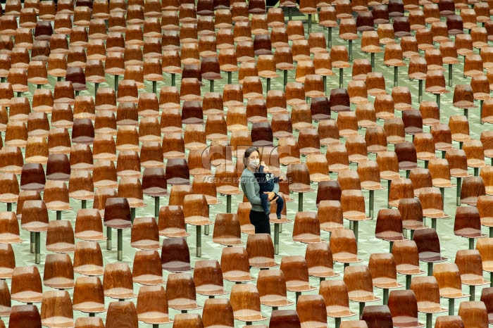 Une femme, son bébé dans les bras, marche au milieu de chaises vides.