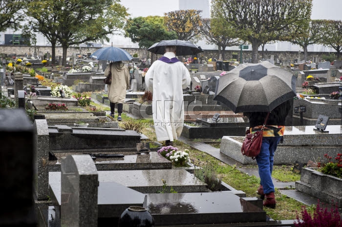 Fête de la Toussaint, prêtre et familles priant au cimetière.
