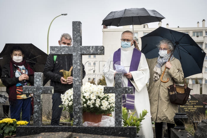 Fête de la Toussaint, prêtre et familles priant au cimetière.