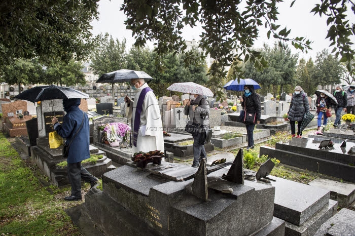 Fête de la Toussaint, prêtre et familles priant au cimetière.