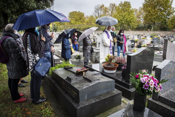 Fête de la Toussaint, prêtre et familles priant au cimetière.