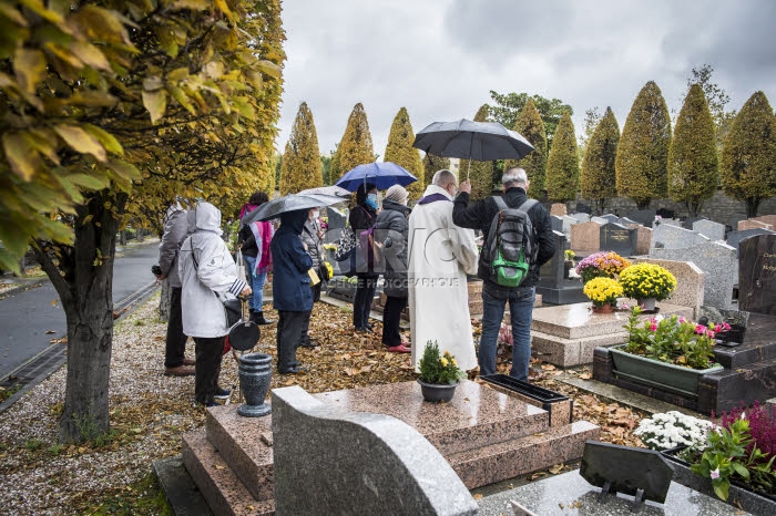 Fête de la Toussaint, prêtre et familles priant au cimetière.