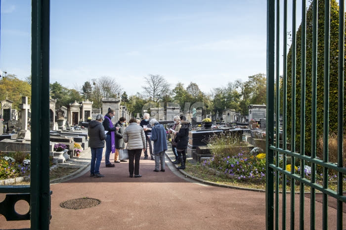 Fête de la Toussaint, prêtre et familles priant dans un cimetière.